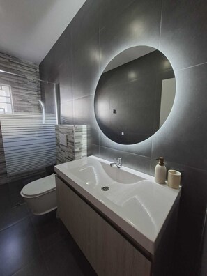 A modern bathroom with a large sink, a toilet, and a mirror with a circular light. - Charming 3-bedroom, 2-bathroom house with AC in quiet neighborhood in Curaçao (Willemstad)