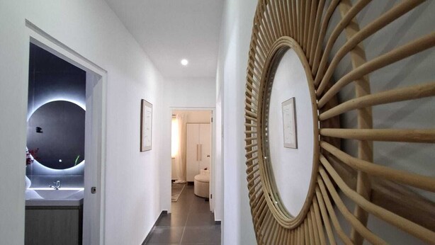A hallway with a modern design, featuring a circular wooden wall art piece and a well-lit sink area. - Charming 3-bedroom, 2-bathroom house with AC in quiet neighborhood in Curaçao (Willemstad)