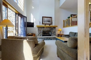 Ein Wohnzimmer mit Kamin aus Stein, zwei Sofas, einem Couchtisch und einem an der Wand befestigten Fernseher.