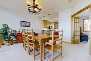 Ein Essbereich mit Holztisch und -stühlen, einer Kristallleuchtre, einem Blumentopf und einer Küche im Hintergrund.