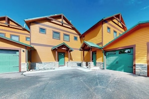 A row of yellow wooden buildings with green doors and garage doors, stone foundations, and a clear blue sky.