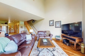 A living room with a brown leather sofa, a wooden coffee table, a TV, and a staircase leading to another level.