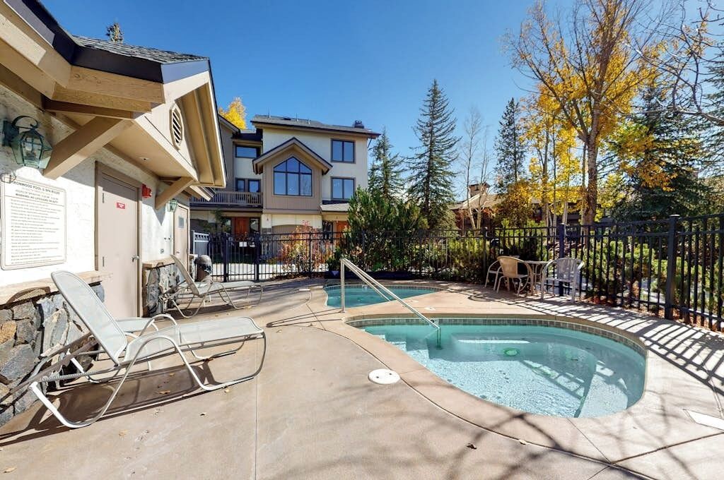 Ein Poolbereich mit Liegestühlen, ein Gebäude mit Balkon und ein eingezäunter Garten.
