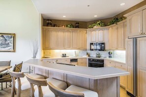 Eine moderne Küche mit Holzschränken, einer zentralen Kochinsel mit Barhocker und einem Essbereich mit Tisch und Stühlen.