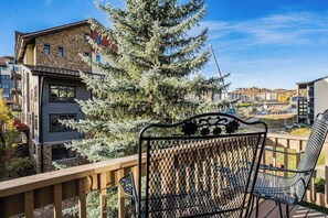 Ein Balkon mit einem Metallstuhl und Blick auf ein Gebäude mit steinverkleideter Fassade und einem Baum.
