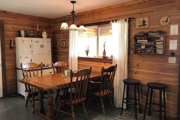 Ein Holzinnenraum mit einem Esstisch, Stühlen, einem Barhocker, einem Kühlschrank und einem fenster mit Vorhängen.