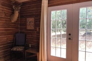 Ein Holzblockhaus-Interieur mit einem Hirschgeweih an der Wand, einem Sessel, einer Tür mit Fenster und einem gerahmten Bild.