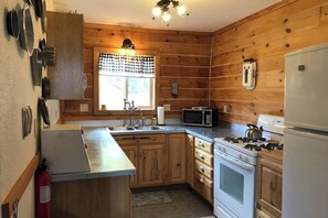 A kitchen with wooden walls, a microwave, stove, and a refrigerator.