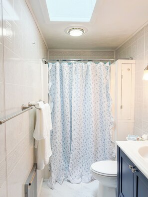A bathroom with a skylight, a toilet, a shower curtain, and a towel rack. - Adorable 2-bedroom cottage less than half a mile from breathtaking Moody Beach (Wells)