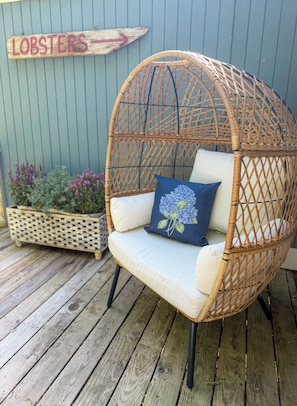 En fletstol med puder, et træskilt og en plantekasse med blomster.