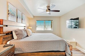 Ein Schlafzimmer mit Bett, Holz-Kopfteil, Deckenventilator, Fenster und Wandbild.