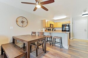 Eine Küche mit Holzschränken, einer Mikrowelle, einem Kühlschrank, einem Esstisch mit Stühlen und einem Deckenventilator.