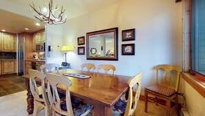 Un comedor con una mesa y sillas de madera, una araña, un espejo y cuadros en la pared.