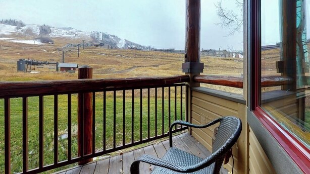 Una terraza de madera con una sola silla de mimbre, con vista a un campo cubierto de hierba y montañas lejanas.