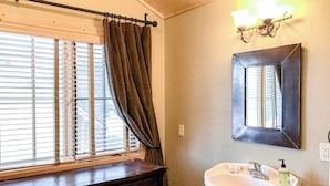 Une salle de bain avec une fenêtre, un lavabo, un miroir et un luminaire.