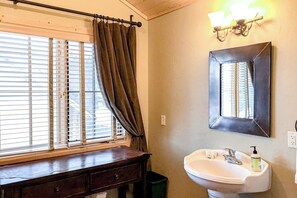 Un baño con ventana, lavamanos, espejo y lámpara.