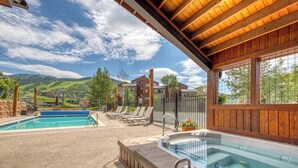 A pool area with a hot tub, lounge chairs, and a view of a mountainous landscape.