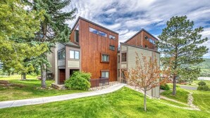 A modern multi-story residential building with a wooden facade, a visible garage, and a well-maintained lawn.