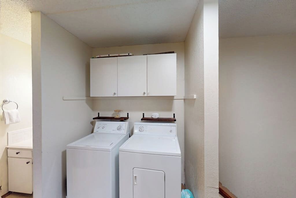 Un lavadero con dos lavadoras y secadoras apiladas, un mueble pequeño en la parte superior y un perchero a la izquierda.