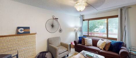 A living room with a fireplace, a sofa, a patterned armchair, a coffee table, and a bicycle decoration on the wall.