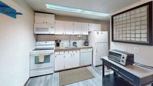 Uma cozinha compacta com armários brancos, micro-ondas, fogão, lava-louças e torradeira.