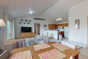 Ein modernes Wohnzimmer mit einer Couch, einem Fernseher, einem Esstisch mit Platzdeckchen, einer Küchenzeile mit einer Mikrowelle und einer kleinen Kochinsel mit Barhocker.