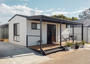 A single-story house with a covered patio, a sliding door, and a small outdoor seating area with chairs. - Clyde C - Family Cabin Sleeps 5 with Bunks (Mollymook)