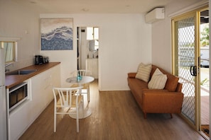 A compact kitchen with a dining table and chairs, a sofa, and a sliding glass door leading to an outdoor area. - Clyde C - Family Cabin Sleeps 5 with Bunks (Mollymook)