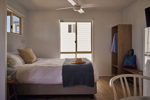 Quarto com cama, ventoinha no teto, janela, guarda-roupa e uma cadeira.