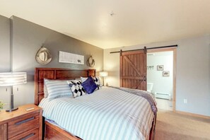 A bedroom with a wooden bed, a nightstand, a lamp, and a sliding barn door. - Mountain condo with full kitchen, fireplace, & deck - close to skiing (Steamboat Springs)