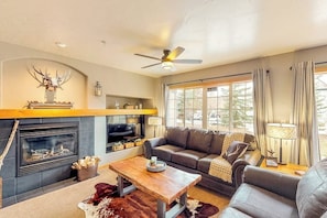 A living room with a fireplace, leather sofa, wooden coffee table, and a ceiling fan. - Mountain condo with full kitchen, fireplace, & deck - close to skiing (Steamboat Springs)