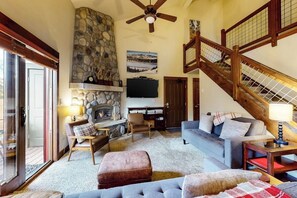 Ein Wohnzimmer mit Kamin aus Stein, Fernseher, einer Couch und einer Treppe.