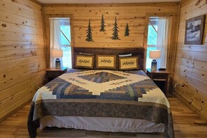 Ein Schlafzimmer in einer Holzhütte mit einem Bett, gerahmten Bildern an der Wand und einem Fenster mit Vorhängen.