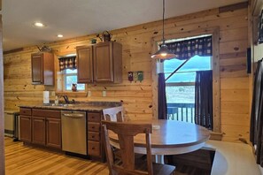 Ein Holzblockhaus-Interieur mit Küche, Essbereich und Blick durch ein Fenster.