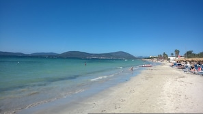 Ein Strand mit klarem Wasser, sandigem Ufer und einigen Personen.