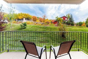 Ein Balkon mit zwei Stühlen, Blick auf ein rotes Haus und eine begrünte Fläche mit Bäumen.