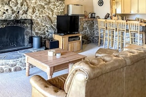 Ein Steinkamin, ein Fernseher, ein Holztisch, ein Ledersofa und eine Steinwand.