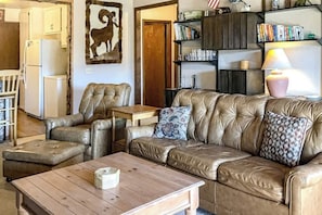 Ein Wohnzimmer mit einer Ledersofa, einem Holztisch und einem Bücherregal mit Büchern und Dekoration.