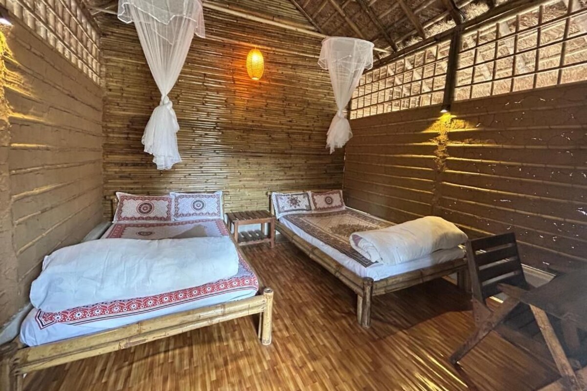 Una habitación con dos camas, piso de madera y techo de paja.