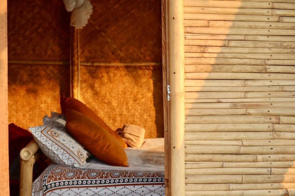 Una cama de madera con ropa de cama estampada y un almohadón, una pared de madera, y un objeto colgante.