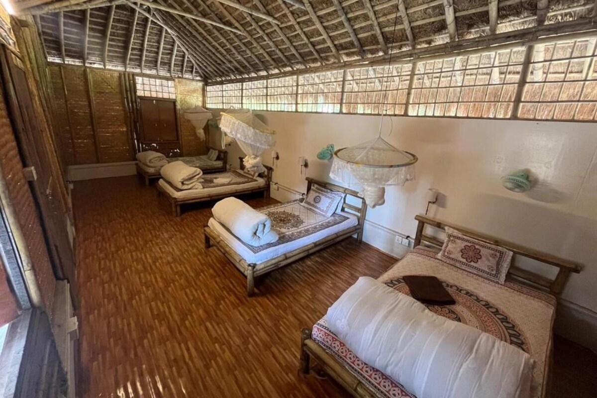 Una habitación rústica con pisos de madera, techo de paja y dos camas de madera con almohadas y mantas.