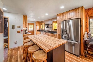 A modern kitchen with wooden cabinets, a stainless steel refrigerator, and a central island with stools. - Spacious home with hot tub, gas grill, fireplace, & washer/dryer (South Fork)