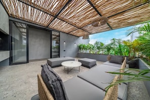 Un patio moderno al aire libre con techo de paja, asientos acolchados y plantas en macetas.