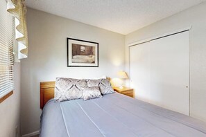 Une chambre à coucher avec un lit, une table de chevet avec une lampe, un tableau encadré au mur et une porte.