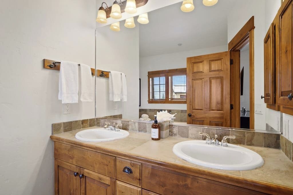 Un baño con dos lavamanos, tocador de madera y un espejo grande.