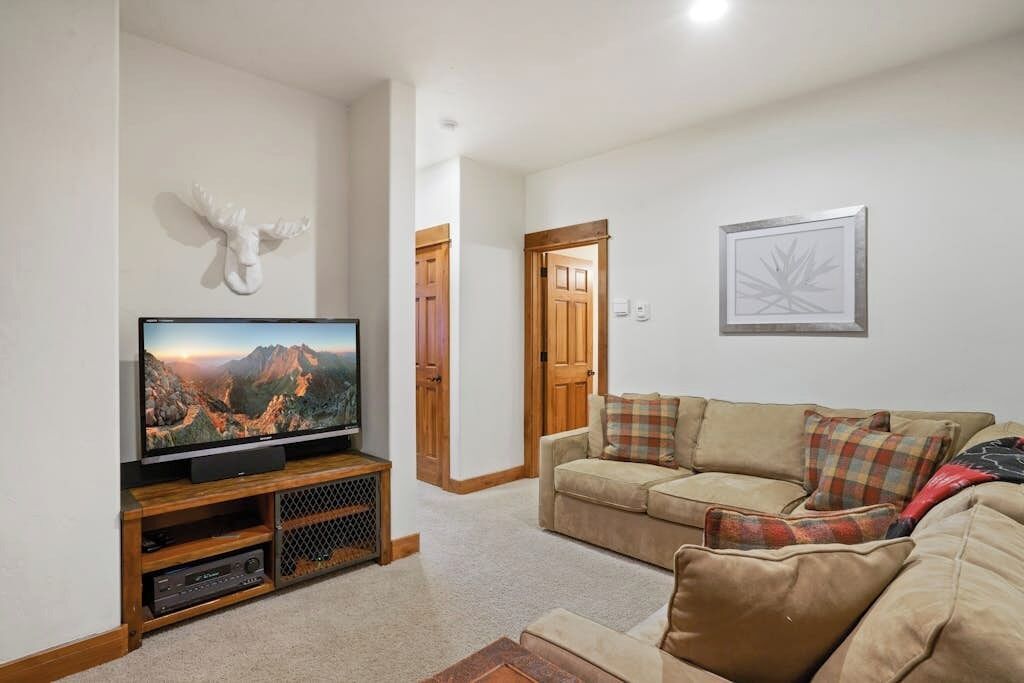 Una sala de estar con televisor, sofá, una puerta de madera y un cuadro enmarcado en la pared.