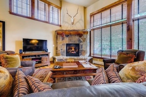 A cozy living room with a stone fireplace, leather sofas, and a mounted deer head. - Walk to the gondola Townhome w/ deck, fireplace, W/D & shared hot tubs/pool (Steamboat Springs)