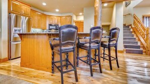 A kitchen with wooden cabinets, a stainless steel refrigerator, and a bar area with four bar stools. - 1442 EagleRidge Walk to the gondola Townhome w/ deck, fireplace, W/D & shared hot tubs/pool (Steamboat Springs)