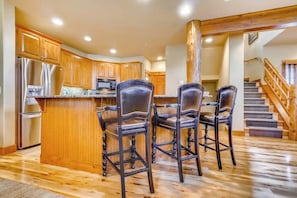 A kitchen with wooden cabinets, a stainless steel refrigerator, and a bar area with four bar stools. - 1442 EagleRidge Walk to the gondola Townhome w/ deck, fireplace, W/D & shared hot tubs/pool (Steamboat Springs)