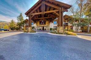 Ein Chalet mit überdachter Veranda, Steinmauern und einem Parkplatz.